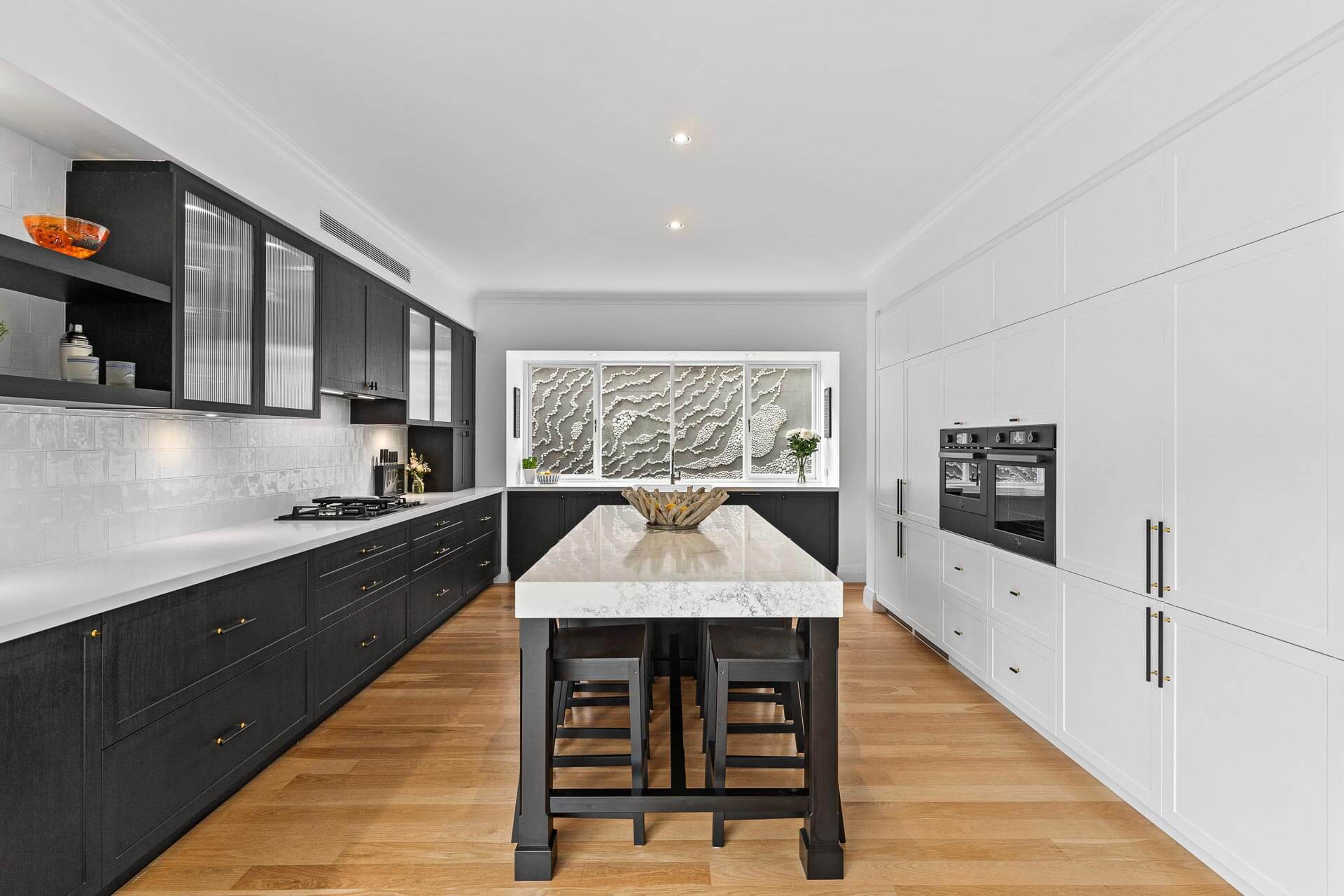 Contemporary closed concept kitchen featuring a marble island with seating, black lower cabinetry, white wall cabinets and warm timber flooring.