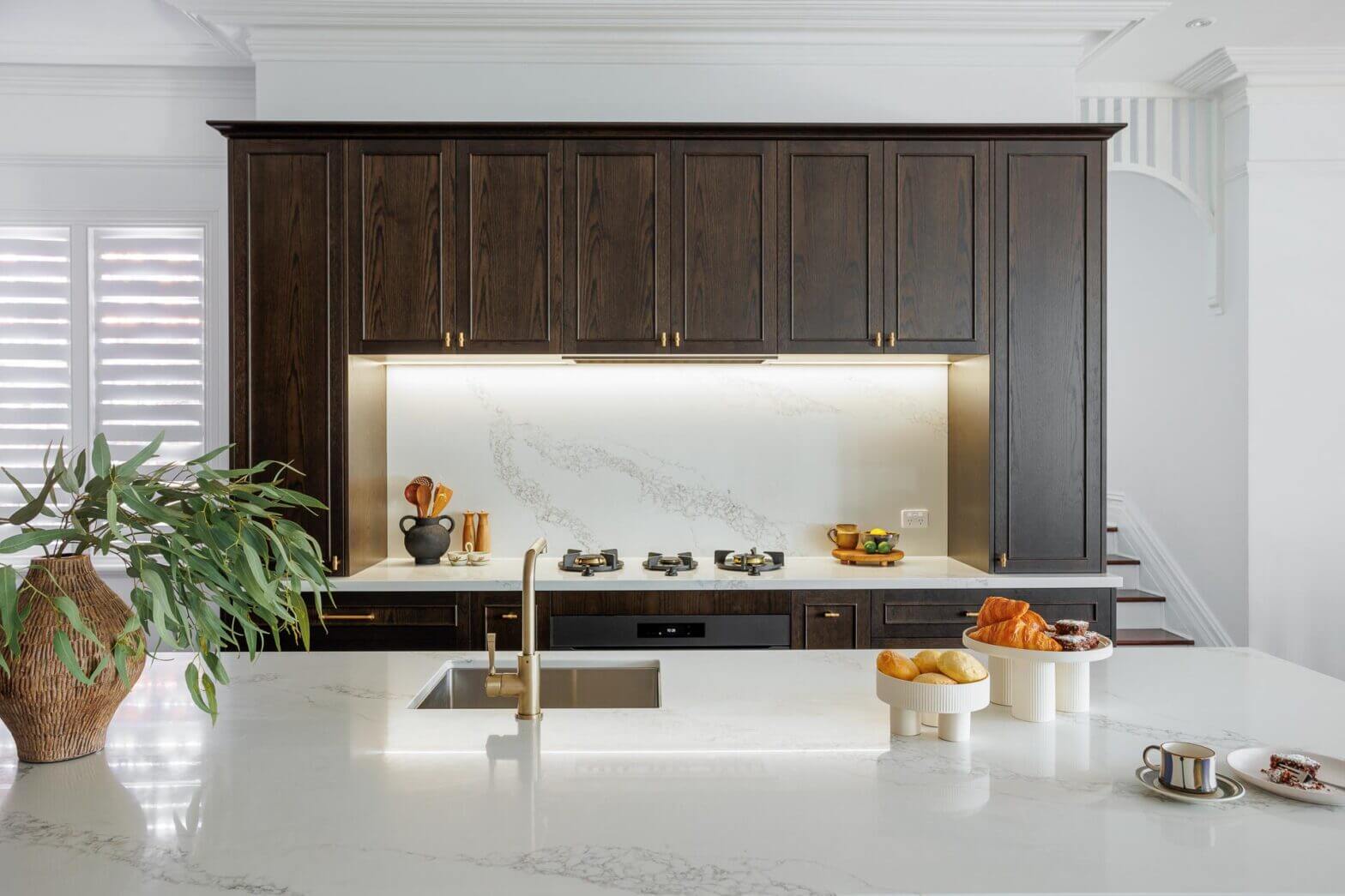 Modern shaker kitchen with dark timber cabinetry, slim framed doors, white stone benchtops and integrated appliances.