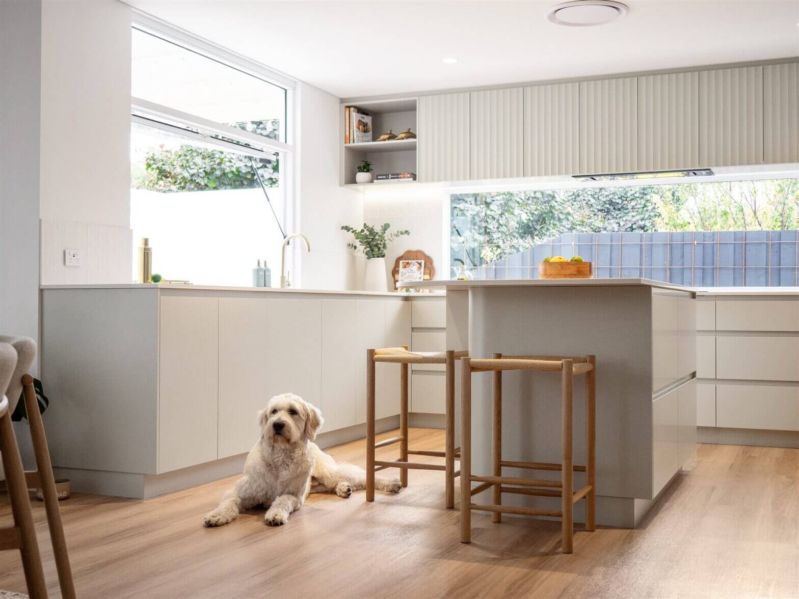 Light-filled modern kitchen with neutral cabinetry, timber flooring and integrated island seating in an open-plan layout