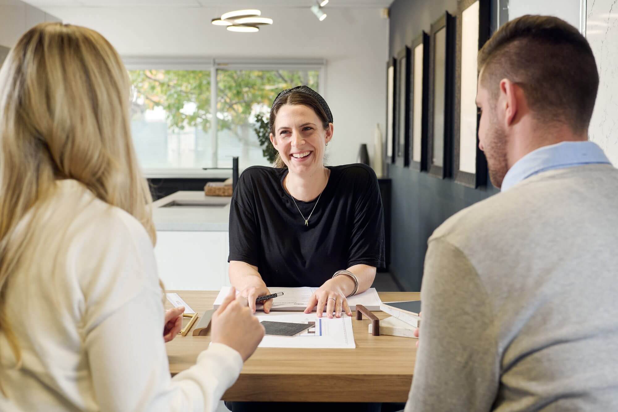 Kitchen design consultation in a showroom setting, with a designer reviewing layout plans and material samples with homeowners