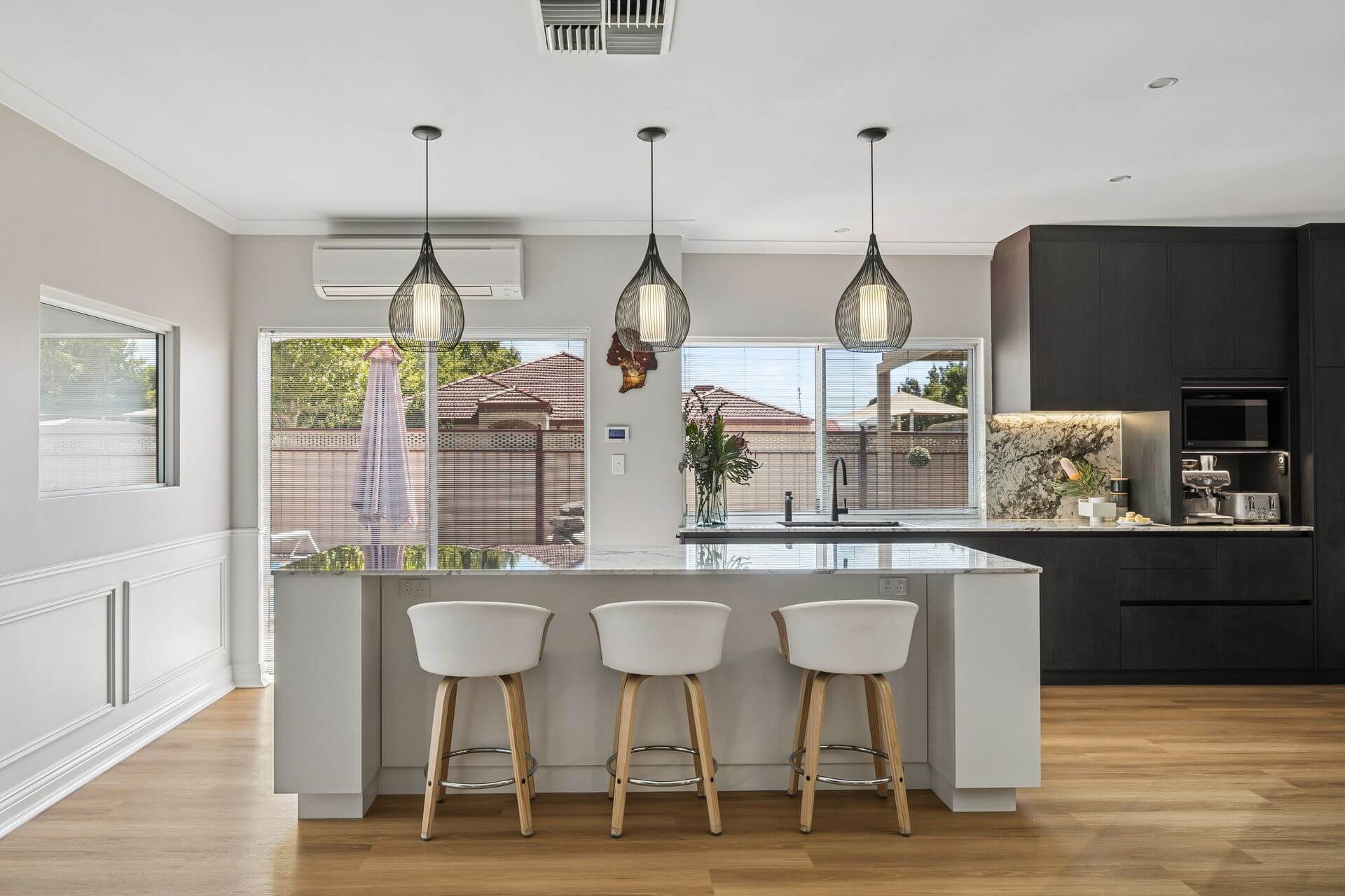 Contemporary kitchen with white island bench, dark cabinetry, pendant lighting and large windows