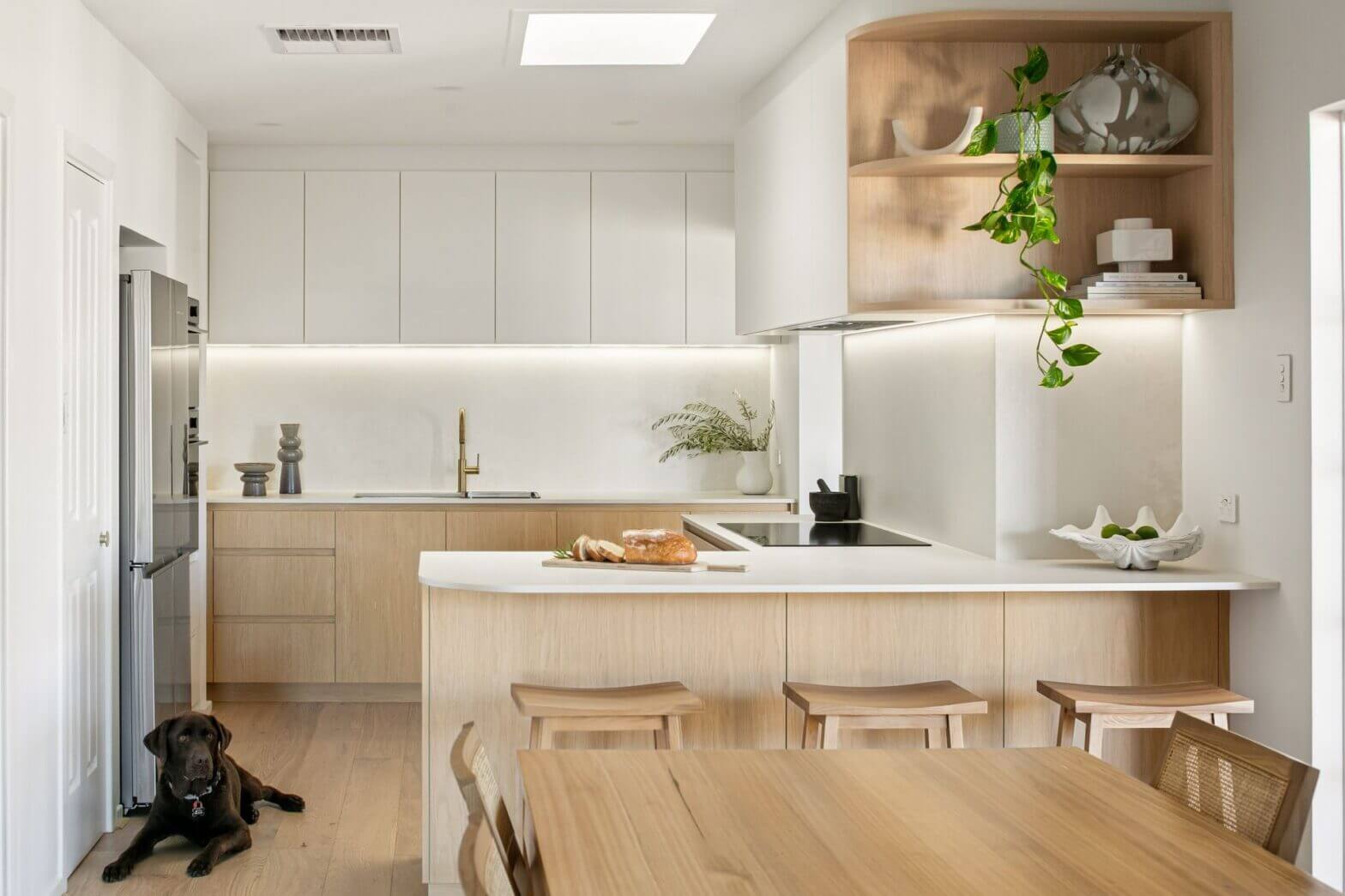 Minimalist kitchen with light timber cabinetry, white countertops, integrated lighting and timber dining area